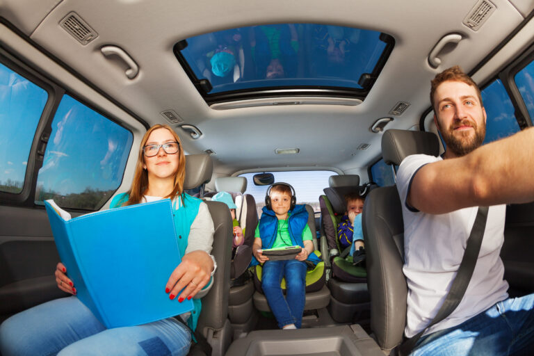 Happy parents traveling by car with three boys, and mother holding book or magazine, inside view